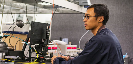 Researcher working at a computer with scientific equipment in a laboratory.