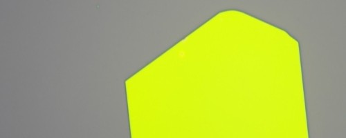Microscope image of a large, bright yellow-green two-dimensional material flake on a grey background