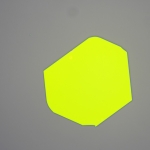 Microscope image of a large, bright yellow-green two-dimensional material flake on a grey background